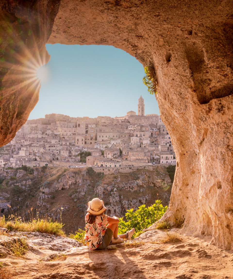 Tourist woman admiring Matera from a cave at sunset, Basilicata, Italy